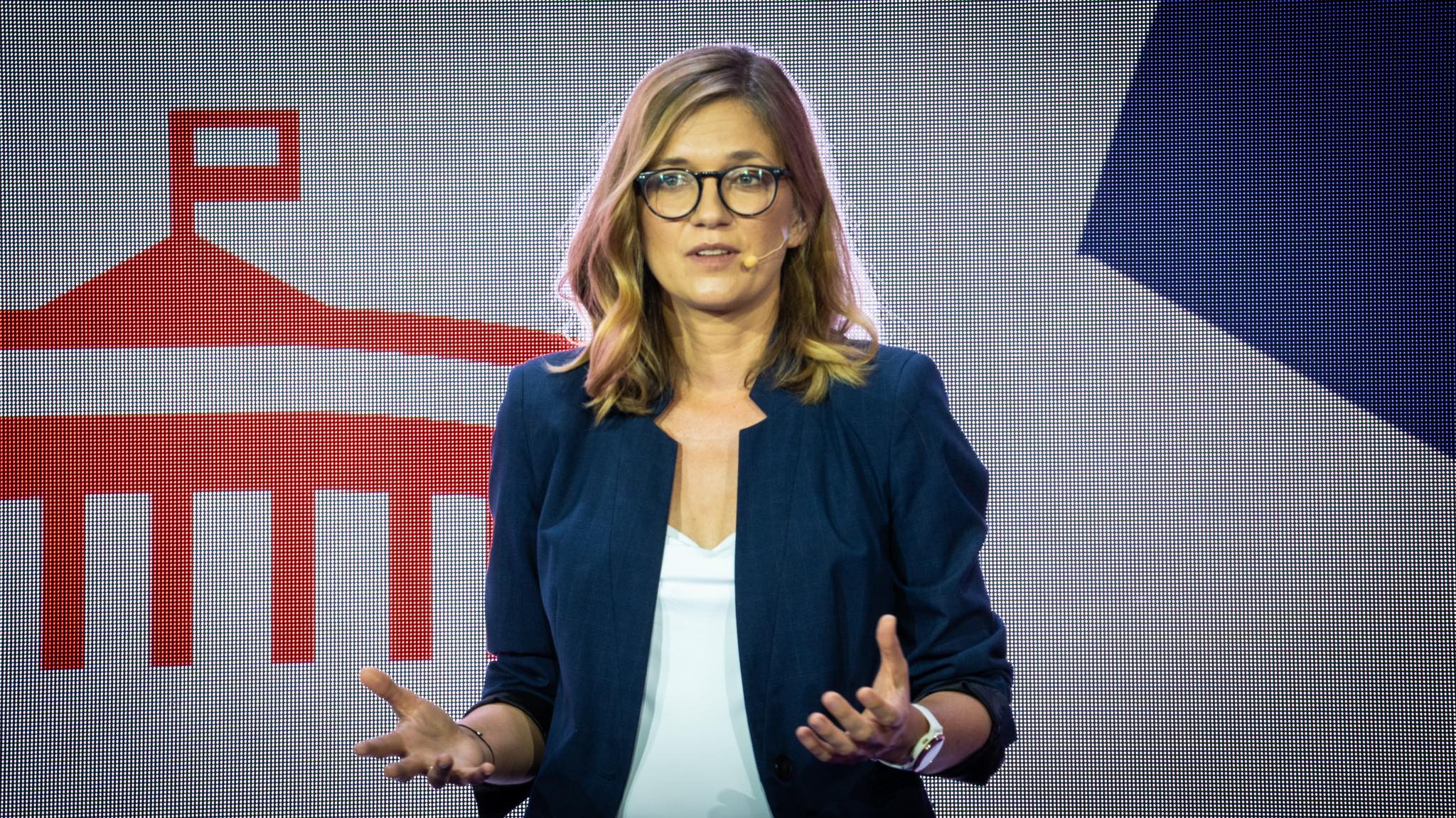 Kobieta z okularami i blond włosami, ubrana w granatową marynarkę, przemawia na scenie podczas wydarzenia „Świeckie państwo – Teraz!”.