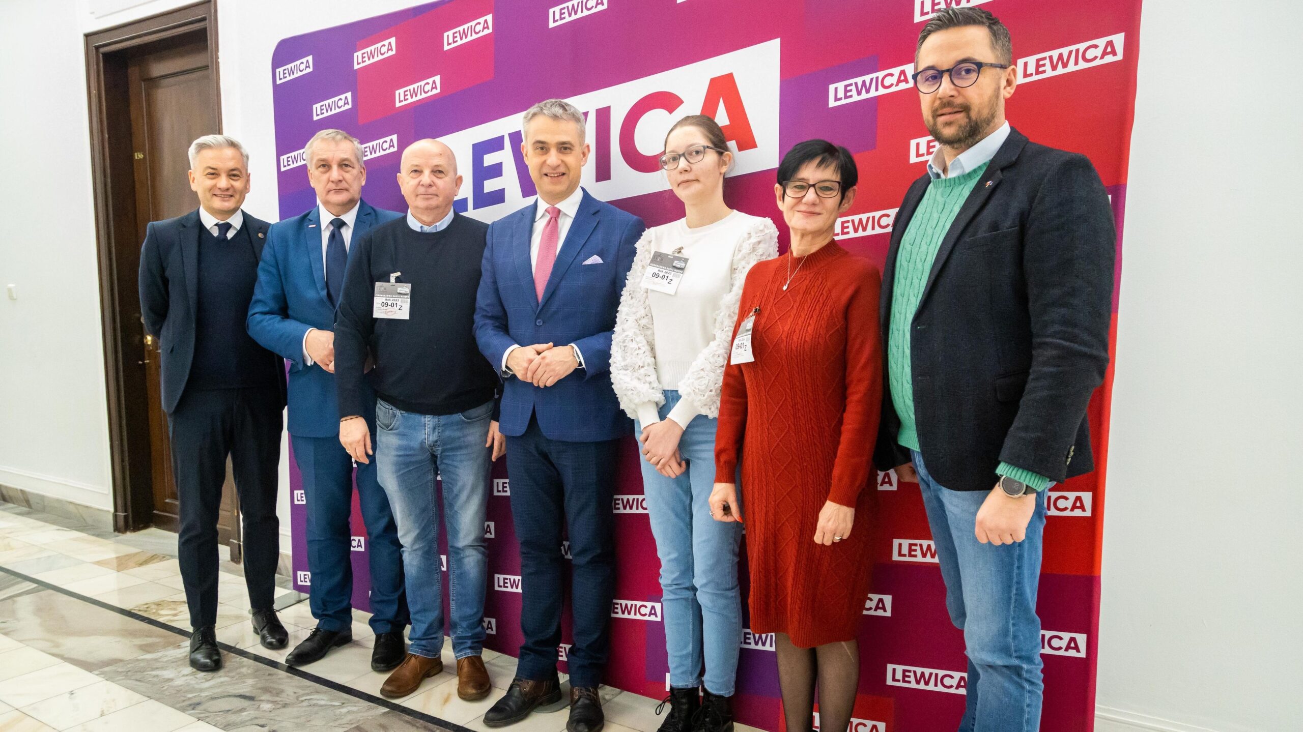 Siedmioosobowa grupa stoi razem przed różowo-fioletowym tłem z logo LEWICA podczas spotkania Bractwa Mundurowego RP.