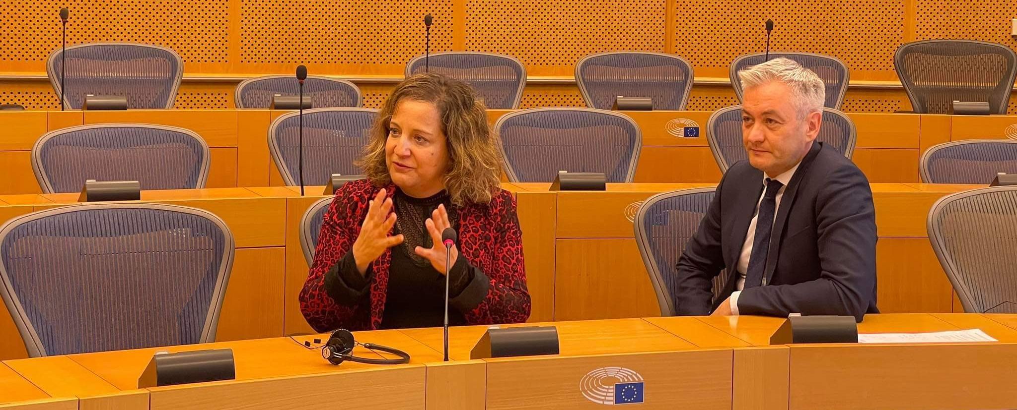 Dwoje ludzi rozmawia w sali konferencyjnej z rzędem pustych krzeseł w tle.