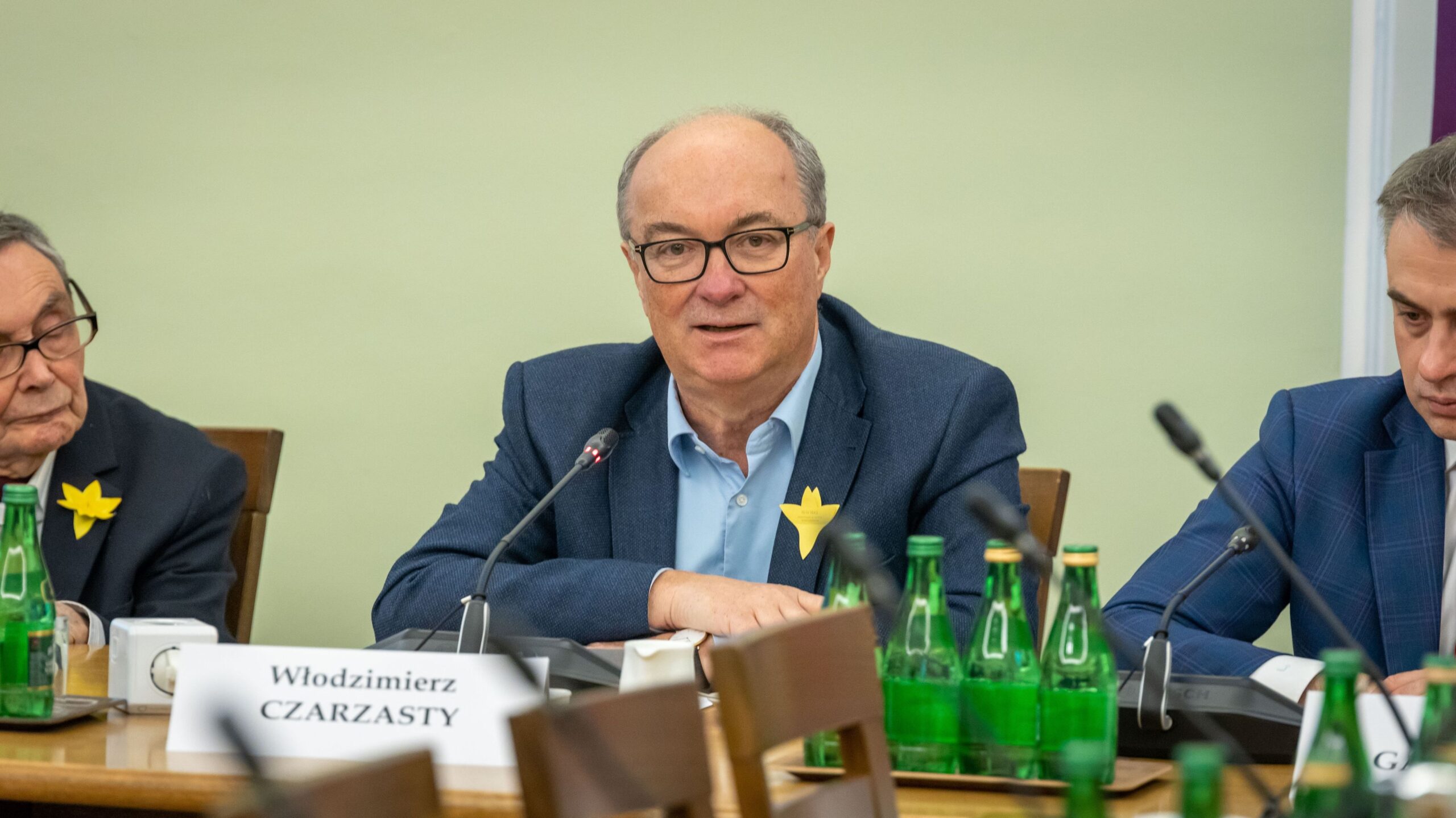 Mężczyzna w garniturze i okularach siedzi przy stole z mikrofonem podczas uroczystej konferencji w Sejmie z okazji 80. rocznicy powstania w getcie warszawskim.