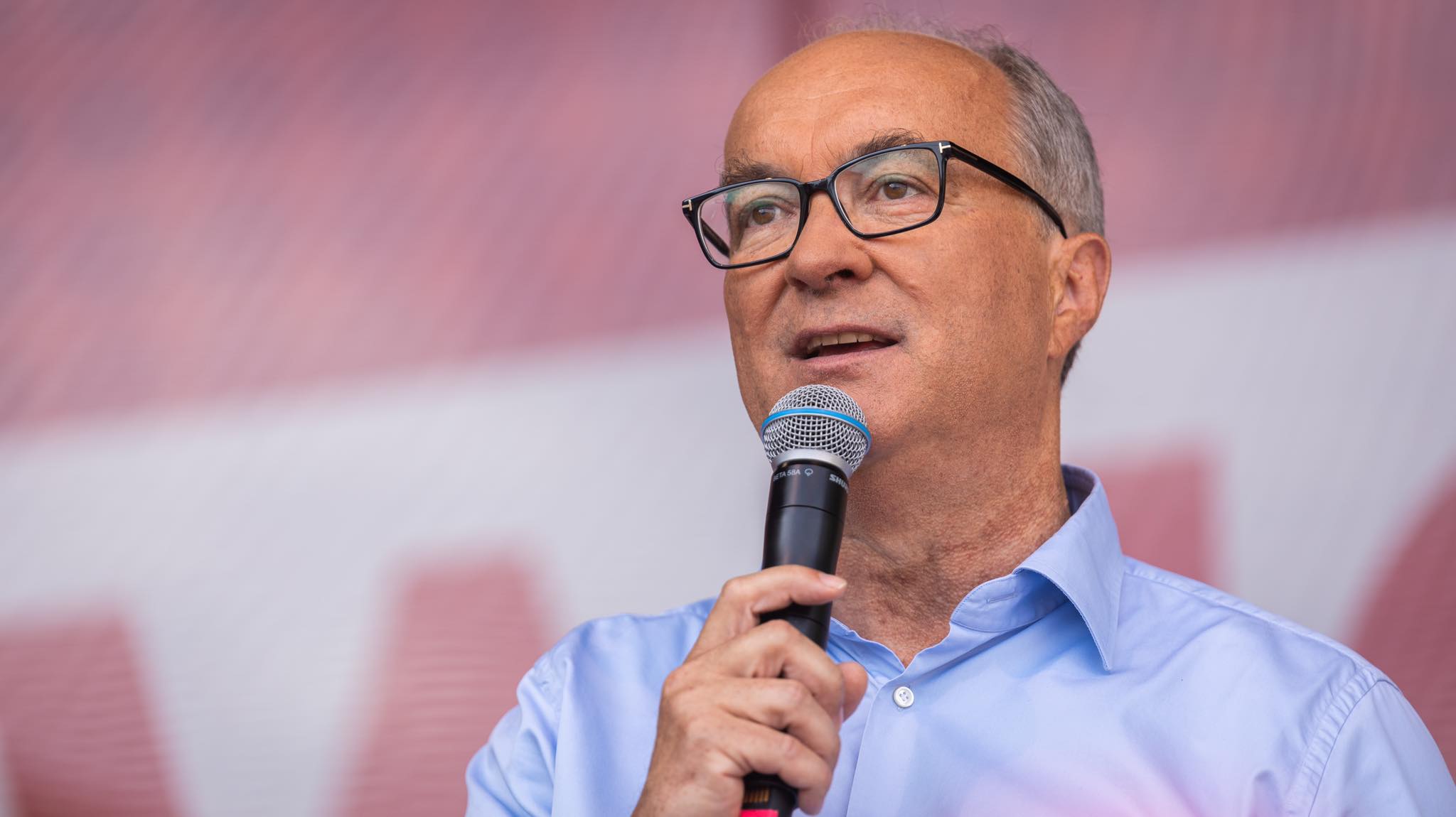 Mężczyzna w okularach i niebieskiej koszuli trzyma mikrofon podczas wiecu w Częstochowie.