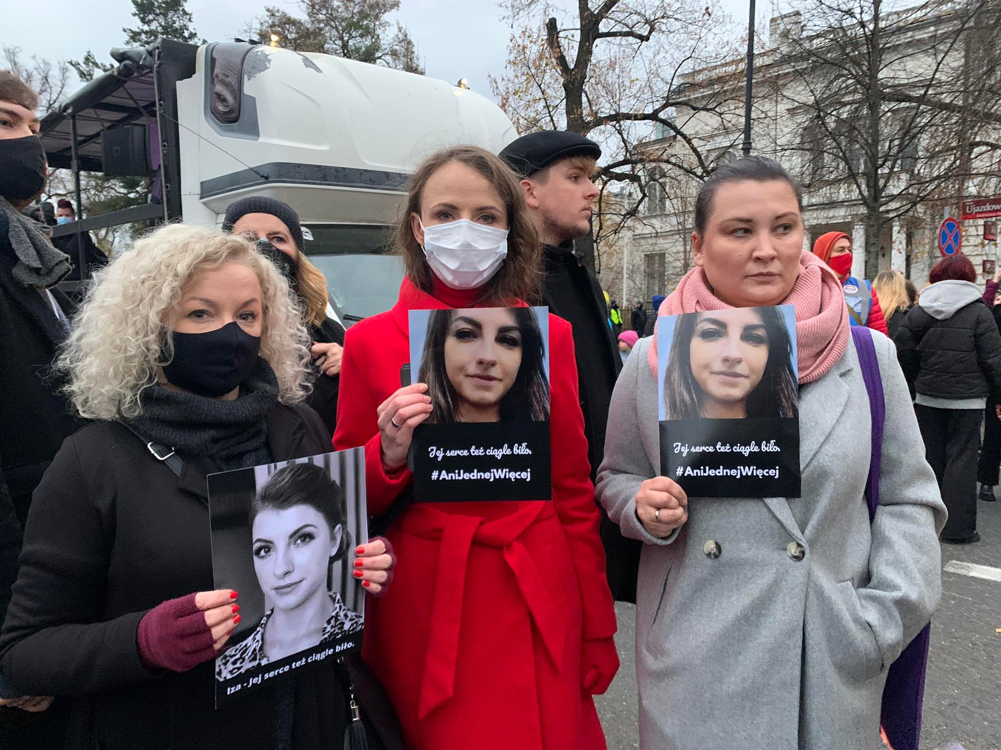 Trzy kobiety stoją na ulicy podczas demonstracji Ani Jednej Więcej, trzymają plakaty z portretami kobiet i hasłami, wszyscy mają maseczki.