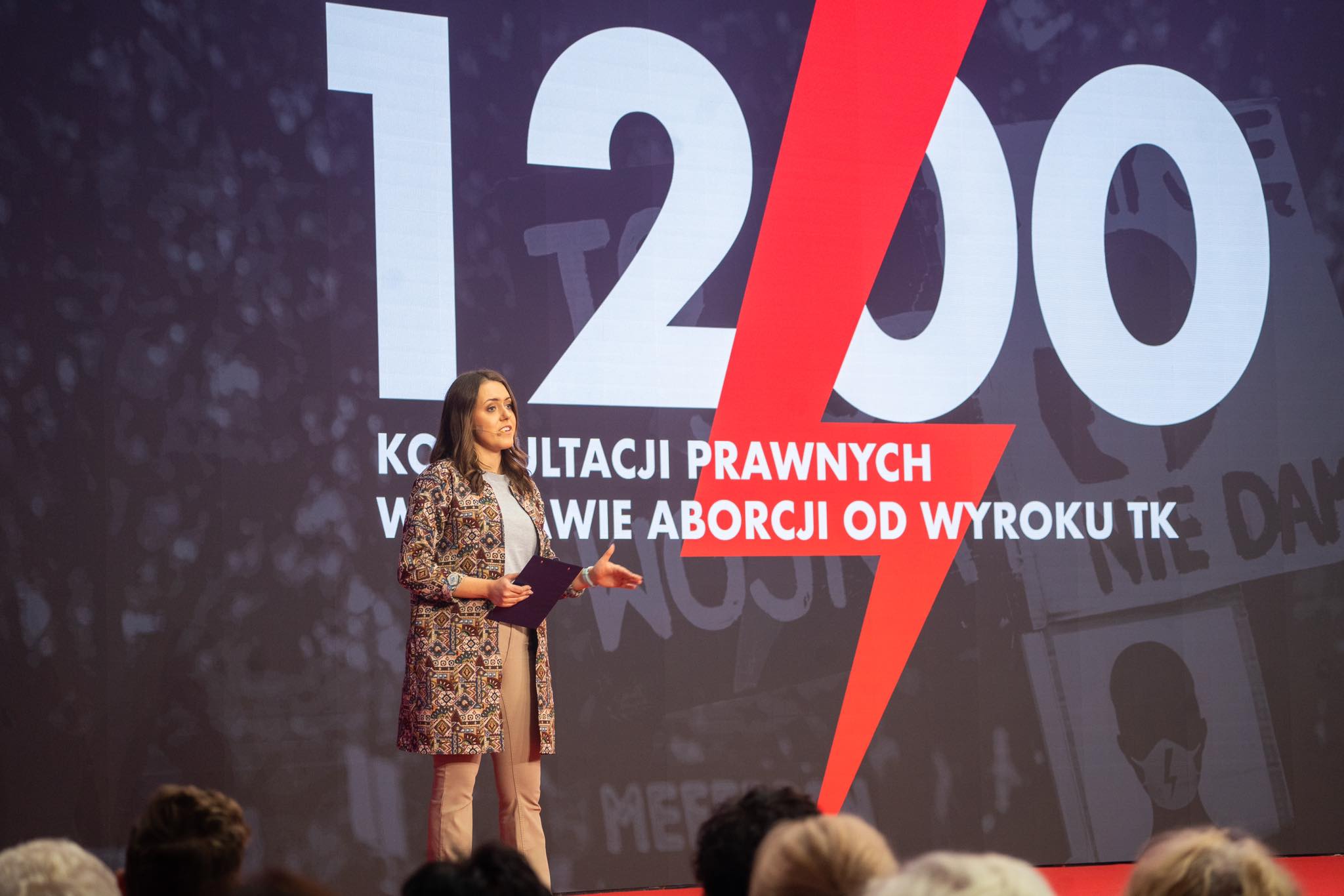 Na zdjęciu przedstawiono kobietę mówiącą na scenie podczas wydarzenia dotyczącego konsultacji prawnych w kontekście aborcji, z dużym napisem