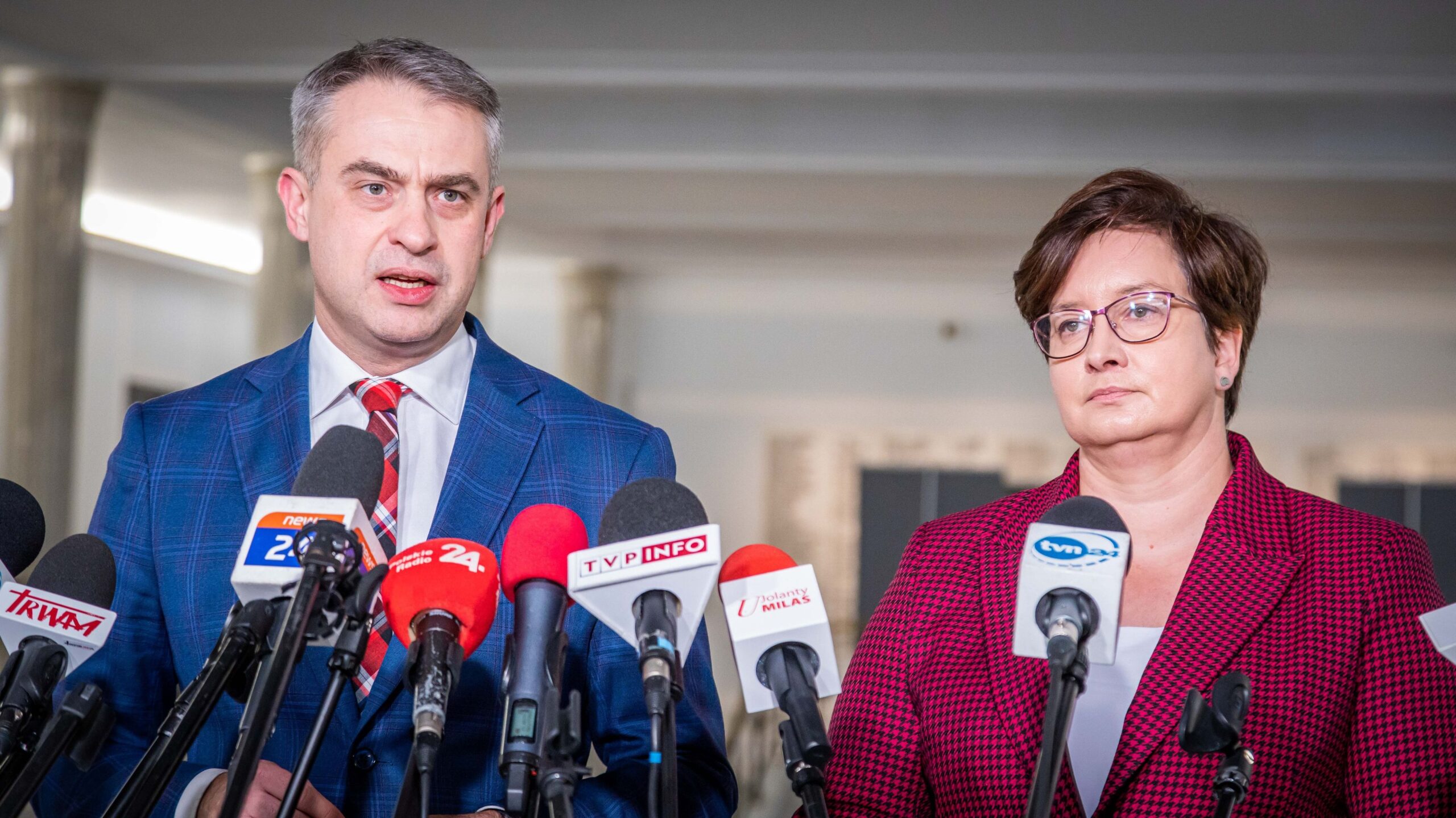 Na zdjęciu widoczna jest para polityków podczas konferencji prasowej, z mikrofonami i kamerami mediów w tle.