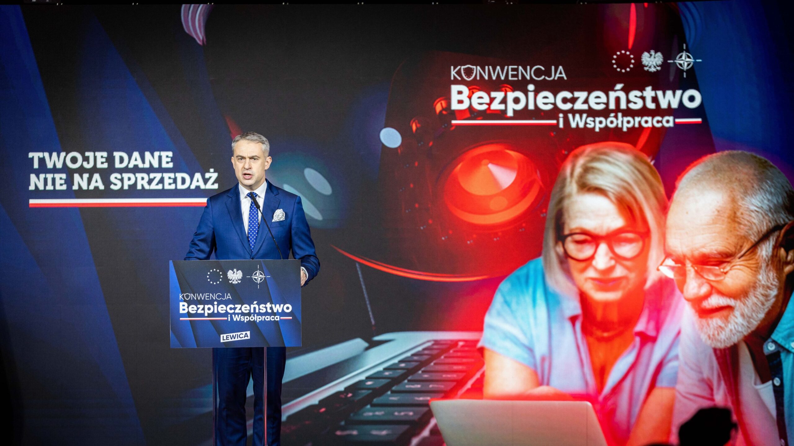 Polityk w granatowym garniturze wygłasza przemówienie na konferencji „Bezpieczeństwo i Współpraca”, a za nim widać tło z hasłem „Twoje dane nie na sprzedaż” i wizerunkami dwóch seniorów przy laptopie, ilustrujące kompleksowy plan wzmocnienia bezpieczeństwa Polski.