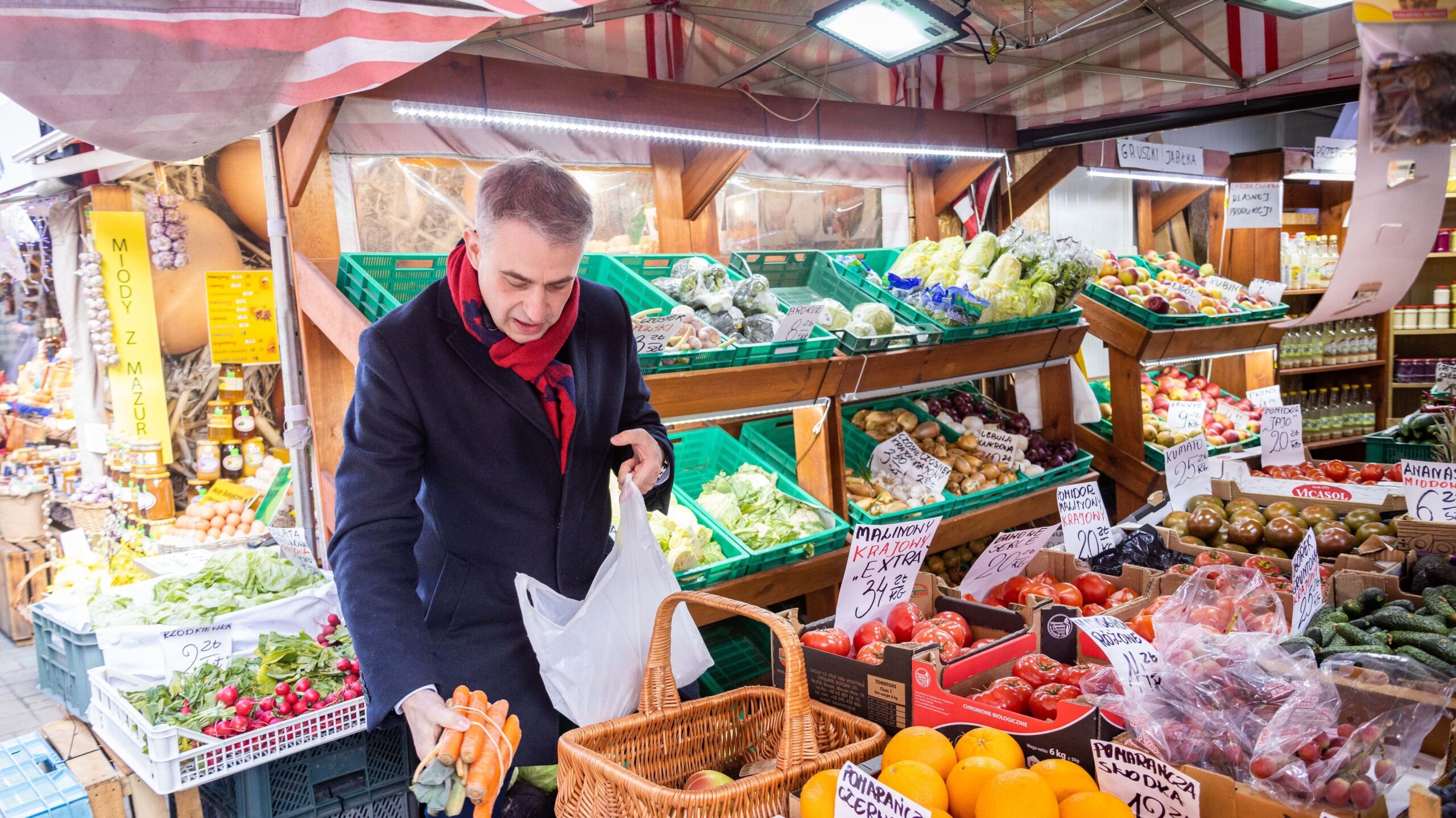 Na zdjęciu widać mężczyznę robiącego zakupy na targu, gdzie sprzedawane są świeże warzywa i owoce.