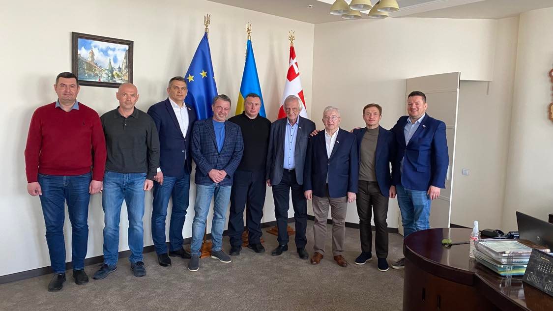 Grupa mężczyzn stojących razem w sali z flagami Unii Europejskiej i Ukrainy w tle, podczas wizyty parlamentarnej w Łucku.