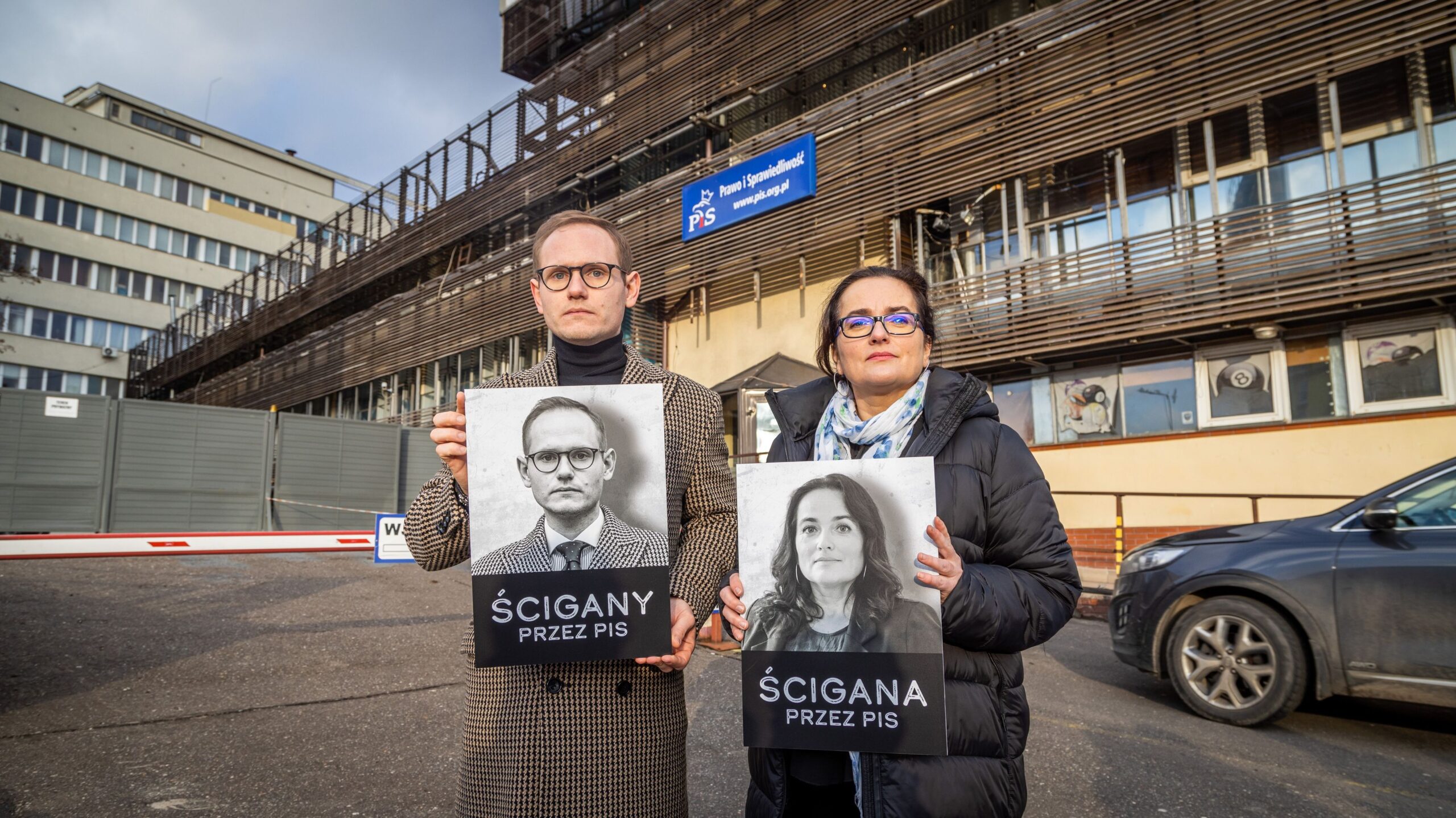 Na zdjęciu widoczni są dwie osoby trzymające plakaty z wizerunkami i napisami 