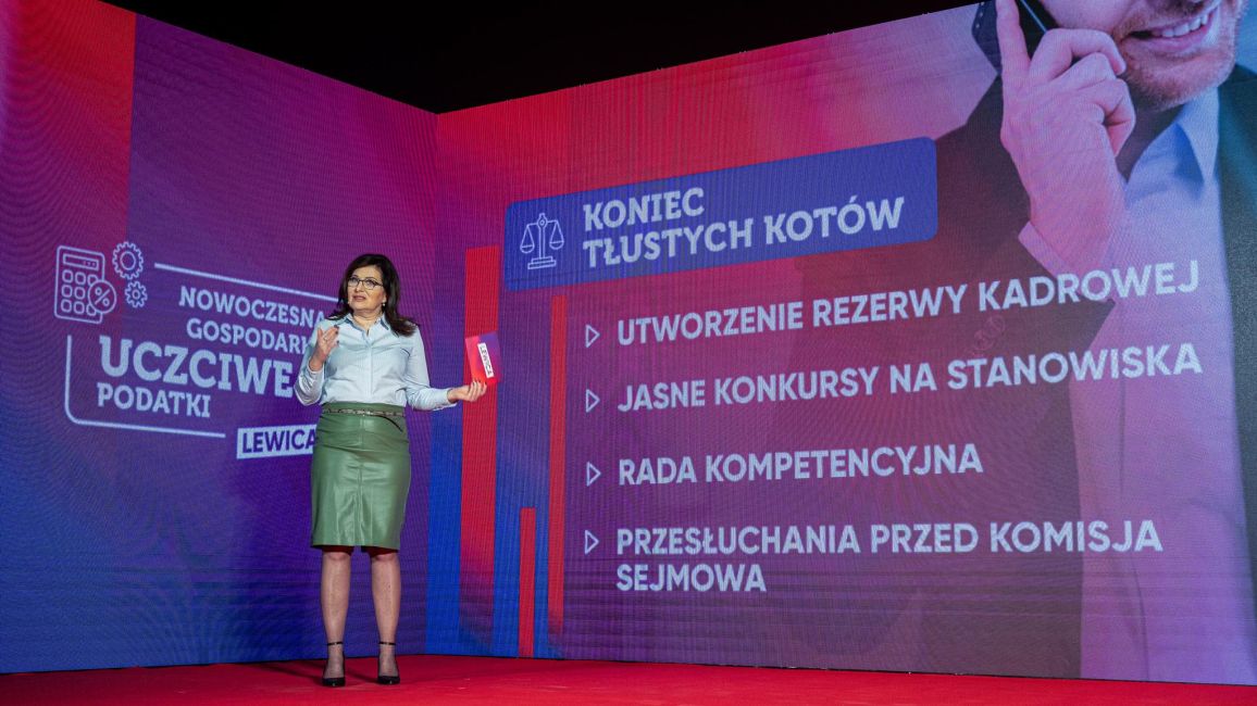 Na zdjęciu widoczna jest kobieta przemawiająca na tle kolorowej prezentacji dotyczącej gospodarki i reform podatkowych.