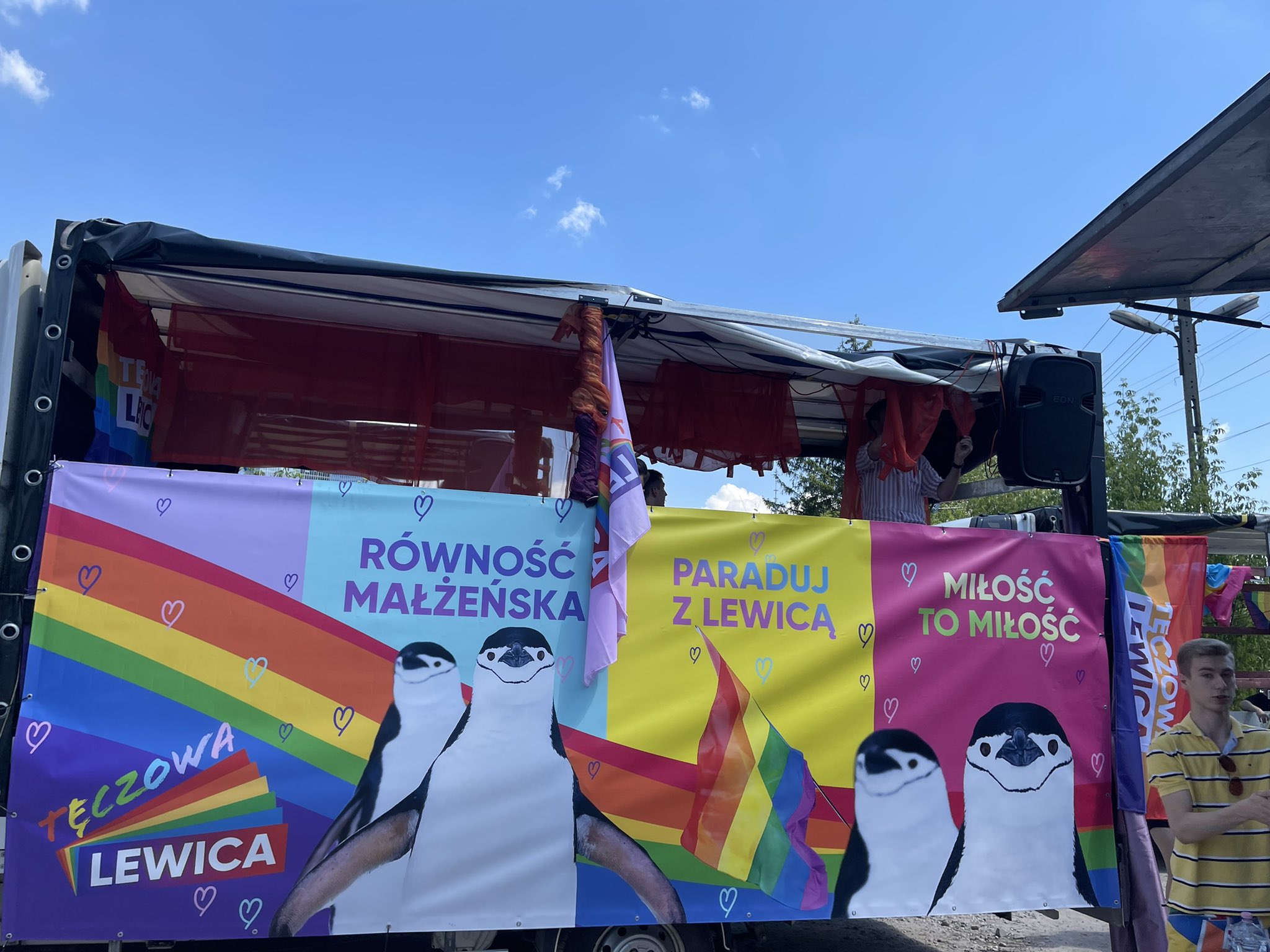 Kolorowy pojaz/platforma na Paradzie Równości 2021 z hasłami „Równość małżeńska” i „Miłość to miłość”, tęczowymi flagami i rysunkowymi pingwinami.