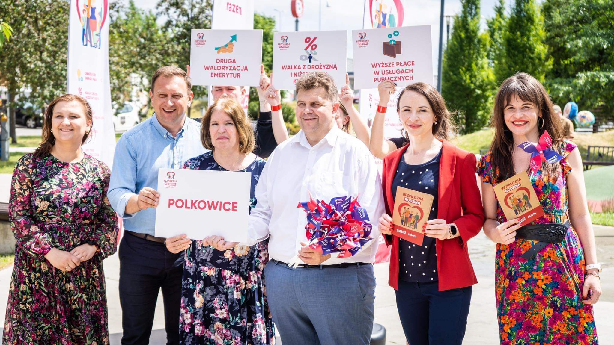Grupa posłów Lewicy na świeżym powietrzu podczas wizyty w Polkowicach w ramach trasy „Bezpieczna rodzina”, trzyma plakaty z hasłami i ulotki.