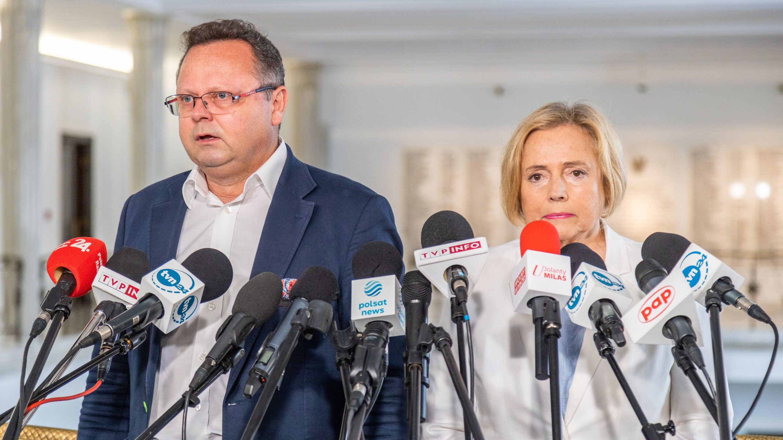 Dwóch polityków stoi przed mikrofonami podczas konferencji prasowej.