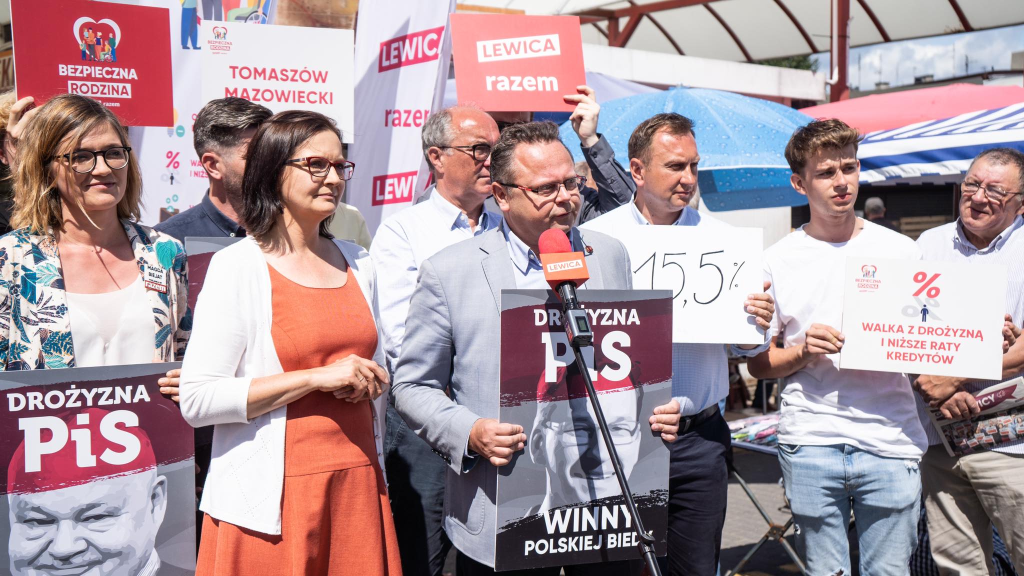 Na zdjęciu grupka ludzi uczestniczy w demonstracji, trzymając transparenty i plakaty z hasłami związanymi z drożyzną i protestem przeciwko rządowi.