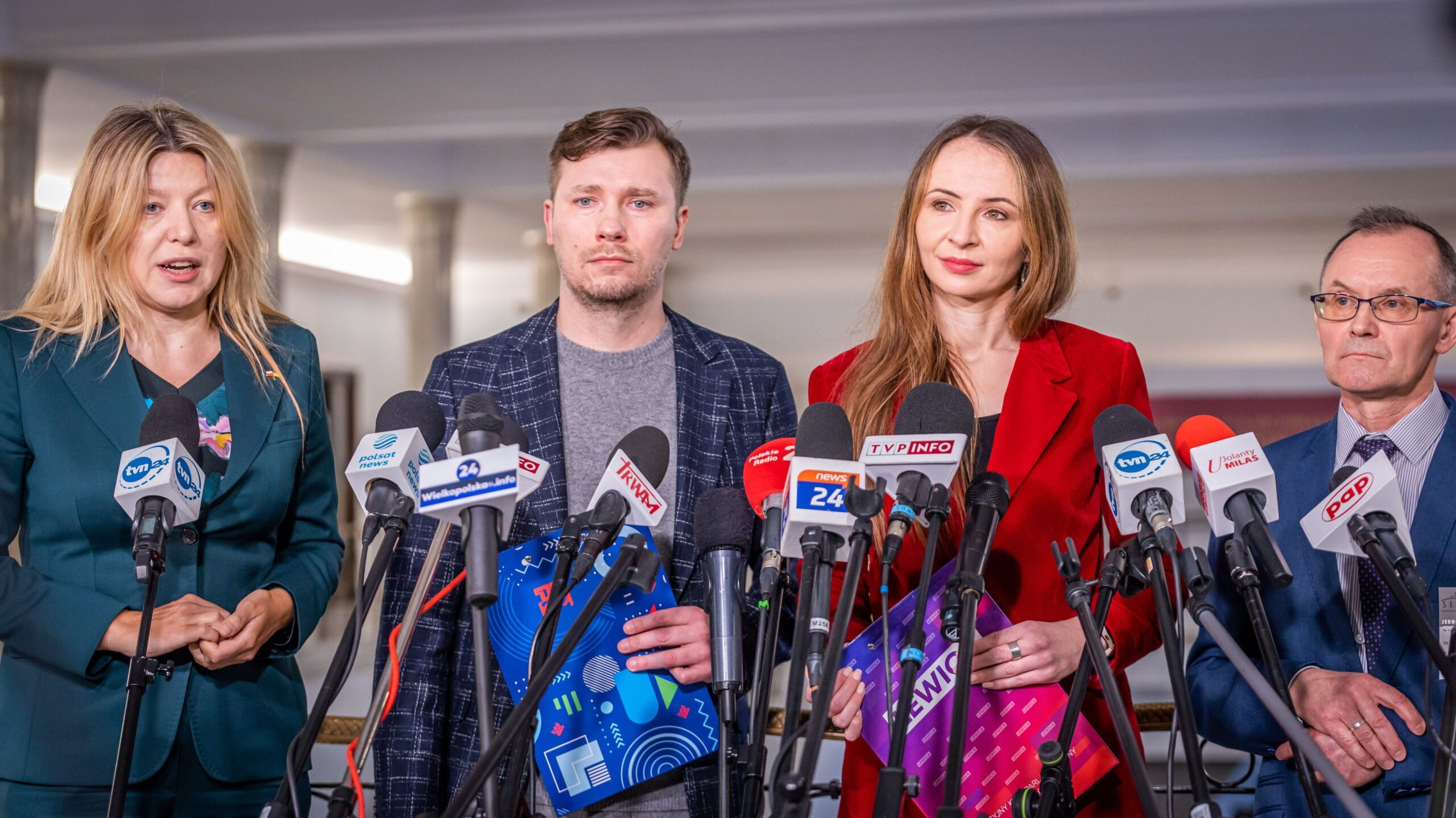 Na zdjęciu widać czwórkę ludzi, którzy stoją za mikrofonami na konferencji prasowej.