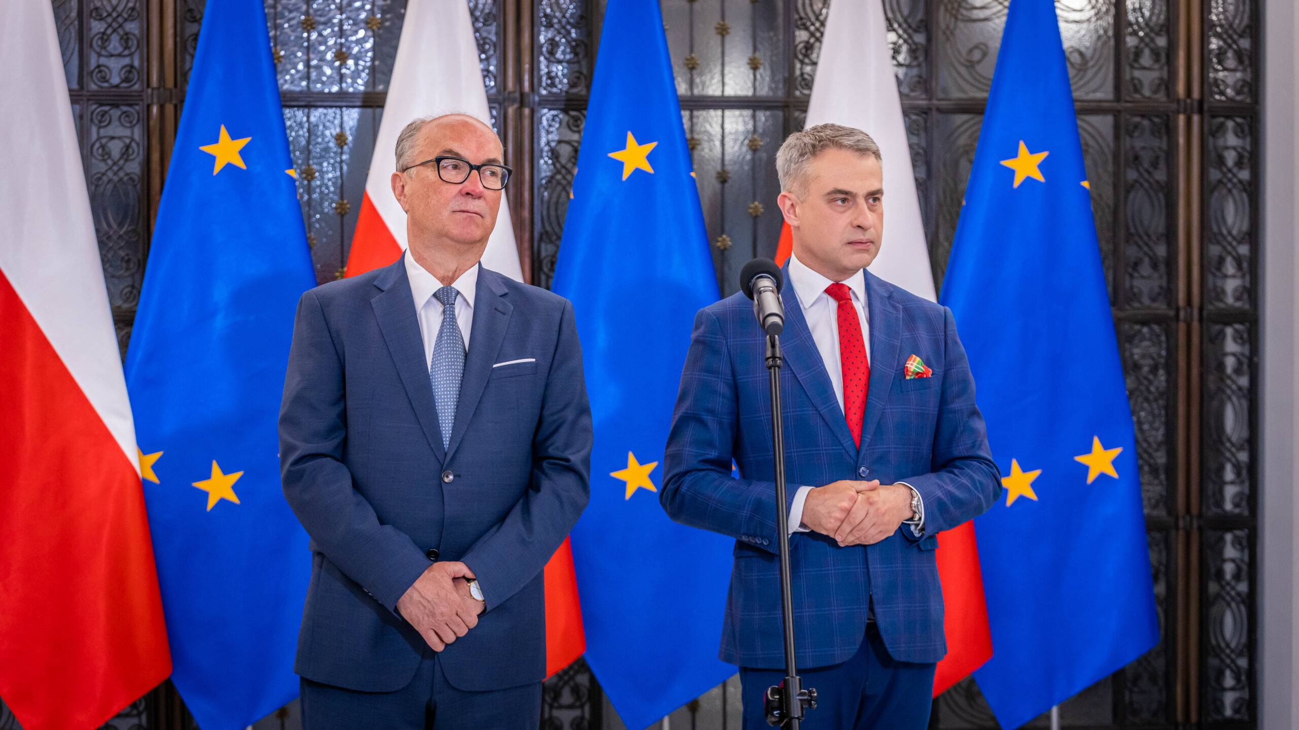 Dwóch mężczyzn w garniturach stoi przy mikrofonie na tle flag Polski i Unii Europejskiej, sygnalizując podpisanie Paktu Sejmowego i gotowość do współpracy.