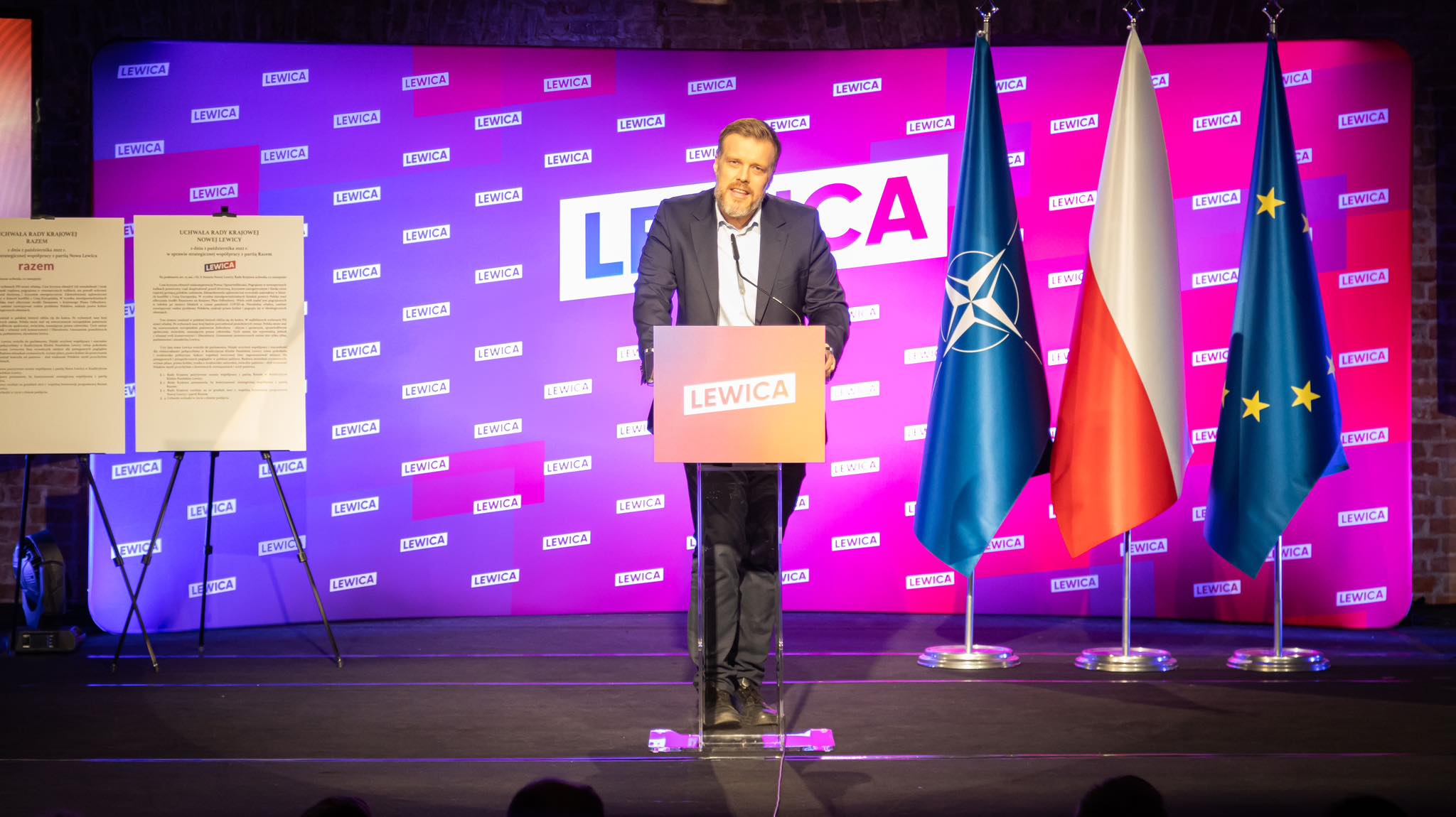 Na zdjęciu widać mężczyznę przemawiającego za mównicą z logo 