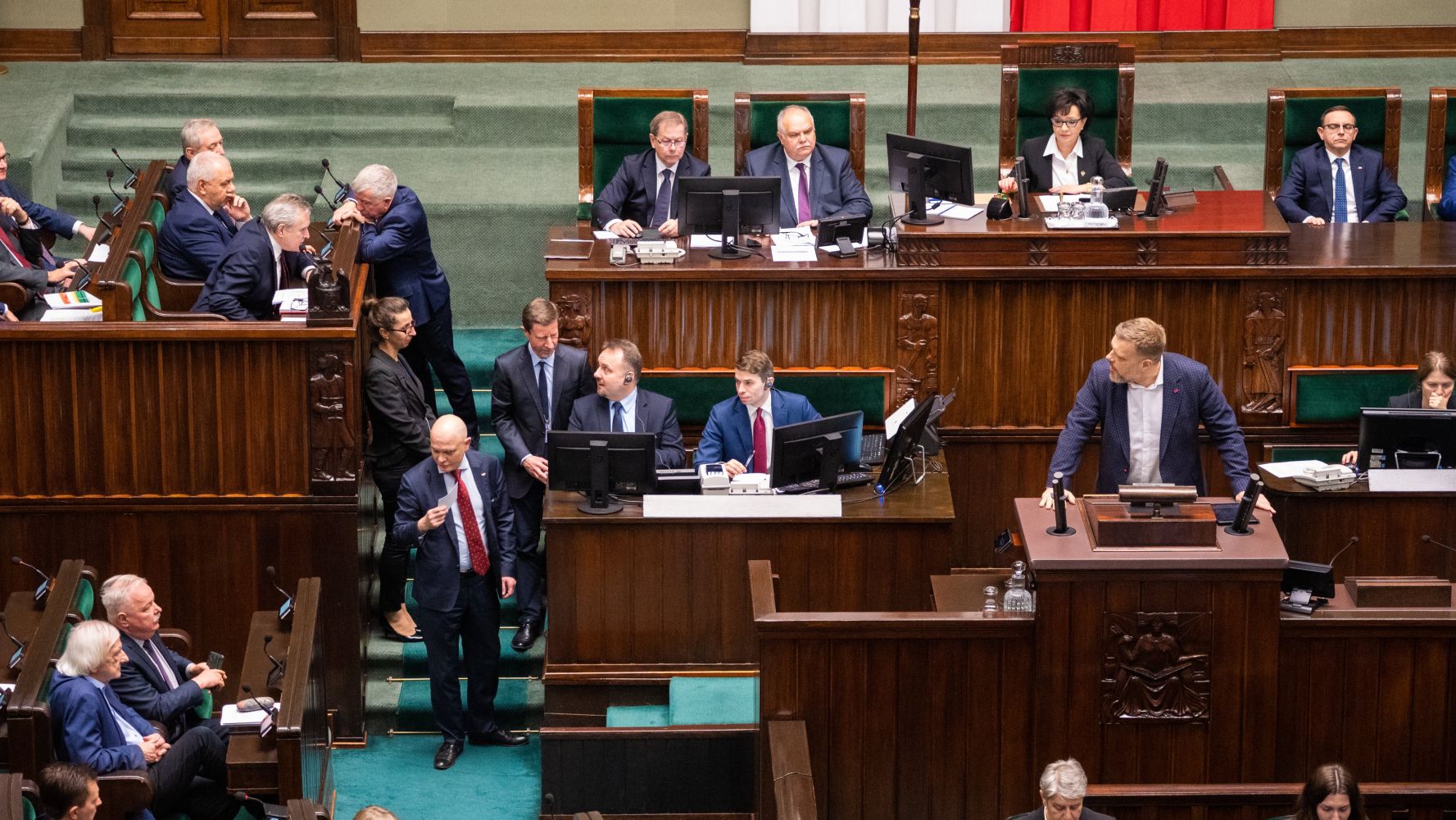 Posiedzenie Sejmu, na którym widać grupę polityków dyskutujących oraz prowadzącego obrady w mównicy.