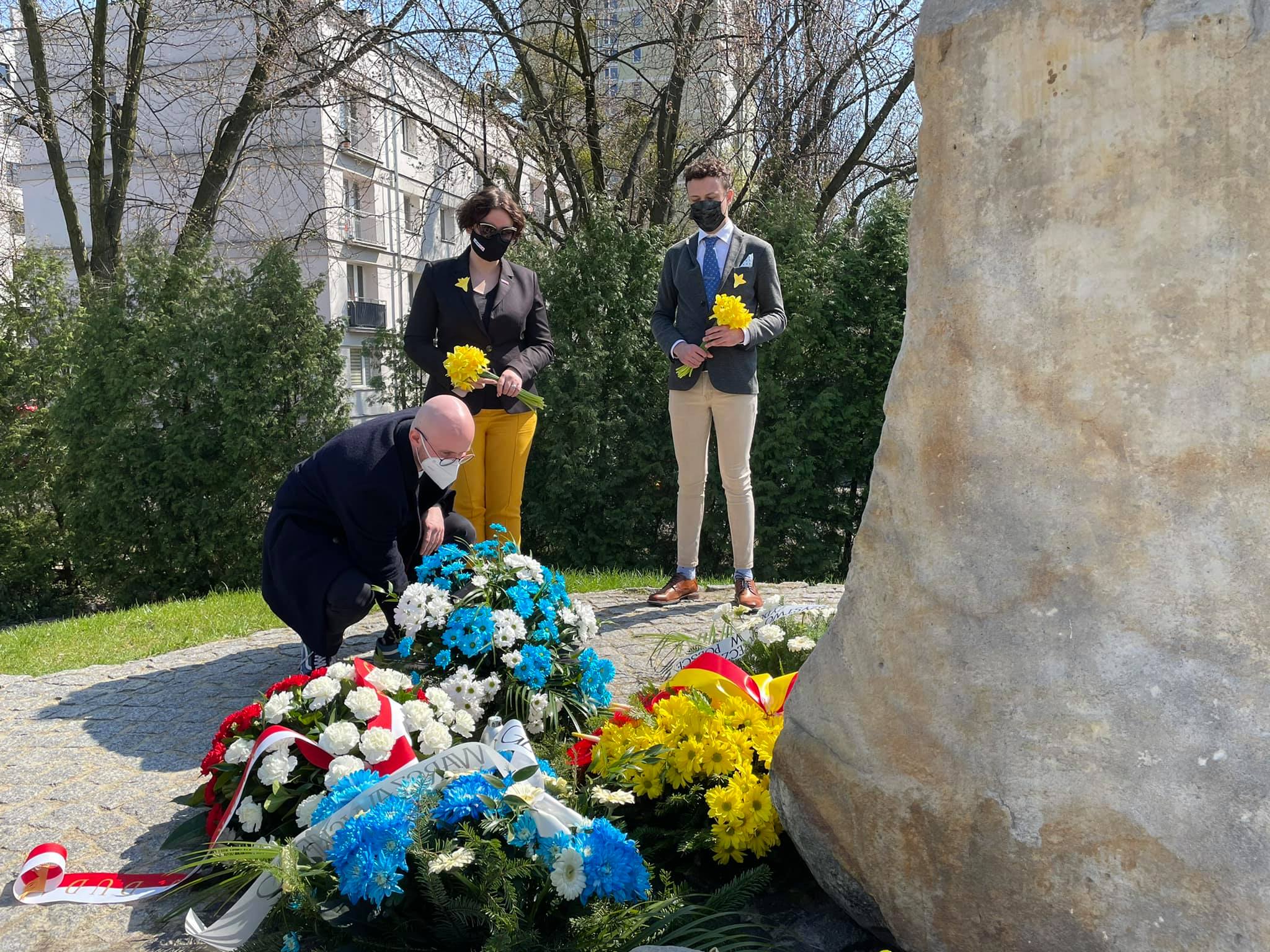 Trójka osób w maseczkach składa kwiaty przy kamiennym pomniku upamiętniającym Powstanie w Getcie Warszawskim podczas obchodów 78. rocznicy.