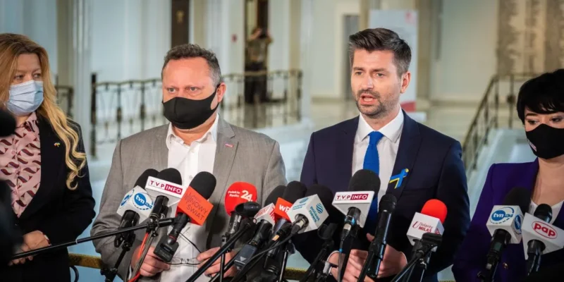 Grupa polityków podczas konferencji prasowej, stojących przed licznymi mikrofonami, omawia projekt likwidacji Izby Dyscyplinarnej.