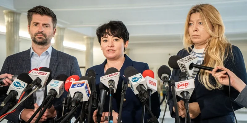 Zdjęcie przedstawia trójkę ludzi stojących za mikrofonami podczas konferencji prasowej.