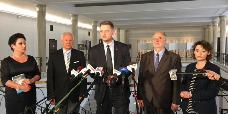 Pięcioro osób stoi za stolikiem z mikrofonami w reprezentacyjnym holu parlamentu podczas konferencji prasowej o ustawie „dezubekizacyjnej”.