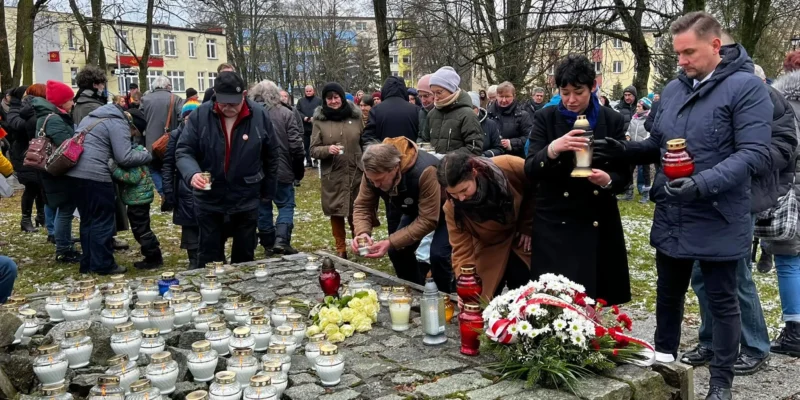 Zgromadzenie ludzi składających kwiaty i zapalających znicze w hołdzie w zamglonym parku.