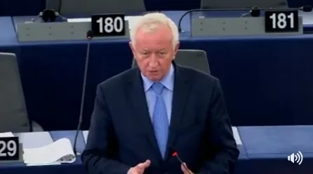 Mężczyzna w garniturze przemawia przy mównicy podczas sesji parlamentu, w tle numery miejsc — wystąpienie dotyczy kwestii transportu.