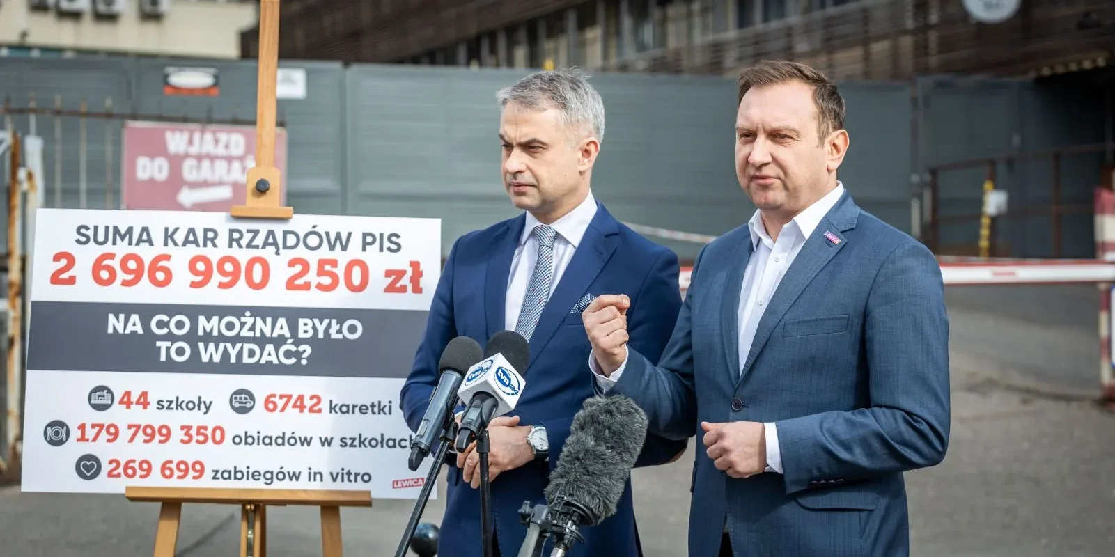 Na zdjęciu dwóch mężczyzn stoi przed tablicą z informacjami o karach rządu PiS i propozycjami, na co mogłyby być wydane te środki.