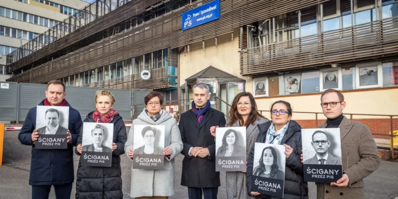 Na zdjęciu widoczna jest grupa osób trzymających plakaty z napisem "ŚCIGANA PRZEZ PiS" przed siedzibą partii.