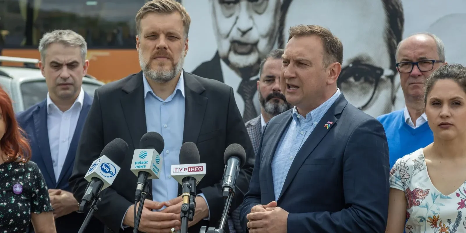 Kilka osób w garniturach przemawia do mediów podczas konferencji prasowej o inflacji w Polsce, stojąc przy mikrofonach.