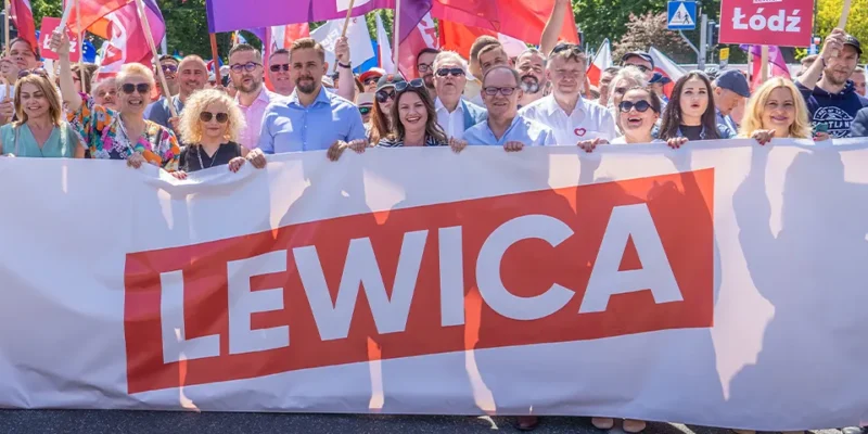 Grupa ludzi na Marszu 4 czerwca trzyma duży baner z napisem LEWICA, otoczona kolorowymi flagami i uśmiechniętymi uczestnikami.