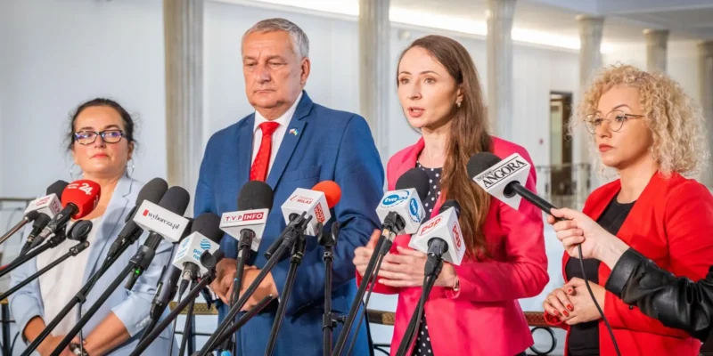 Na zdjęciu widać cztery osoby stojące przed mikrofonami podczas konferencji prasowej.