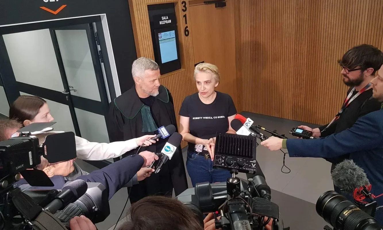 Dwóch polityków udziela wywiadu mediom w korytarzu przy sali rozpraw 327, otoczeni kamerami i reporterami.