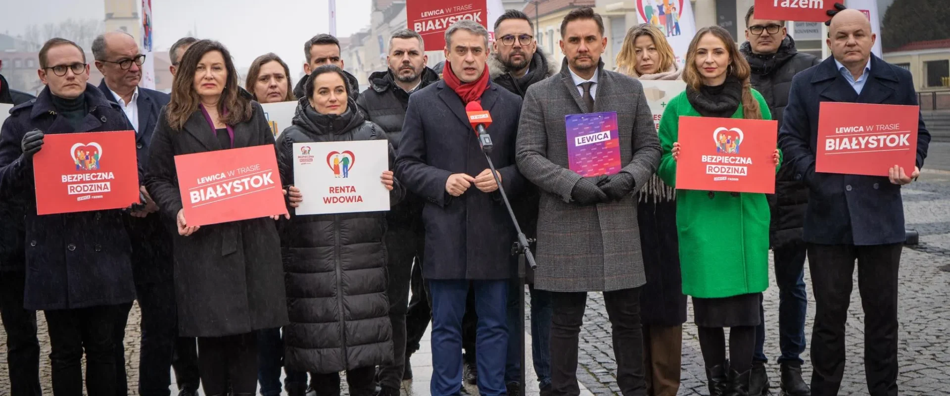 Na zdjęciu grupa osób z transparentami, związana z wydarzeniem w Białymstoku, prezentuje różne hasła polityczne.