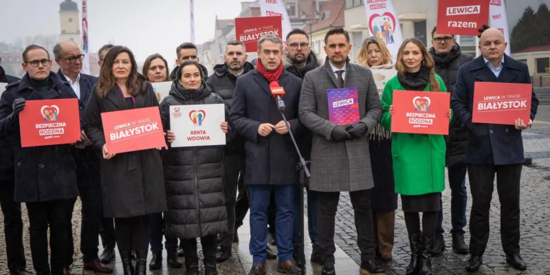 Na zdjęciu grupa osób z transparentami, związana z wydarzeniem w Białymstoku, prezentuje różne hasła polityczne.