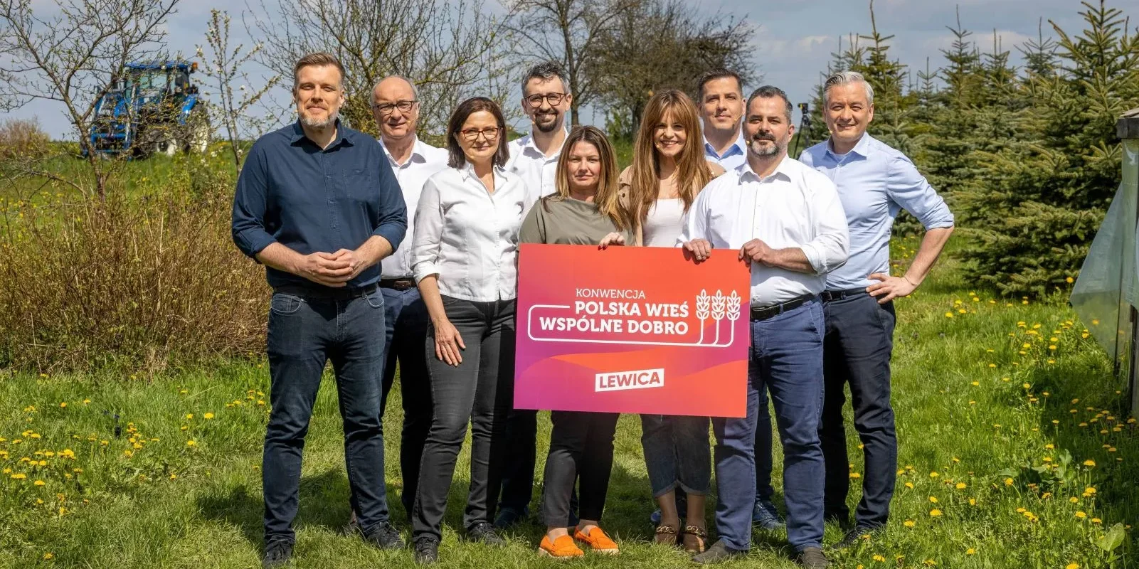Grupa osób stoi na zielonym tle z kwiatami, trzymając banner promujący inicjatywę "Polska Wieś Wspólne Dobro" organizacji Lewica.