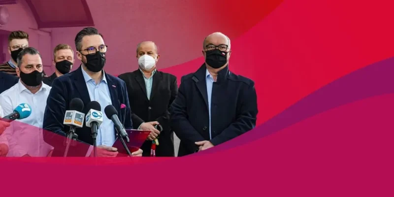 Grupa parlamentarzystów wraz z dziennikarzami podczas konferencji prasowej w Żurominie, przy stojących mikrofonach, wszyscy w maseczkach.