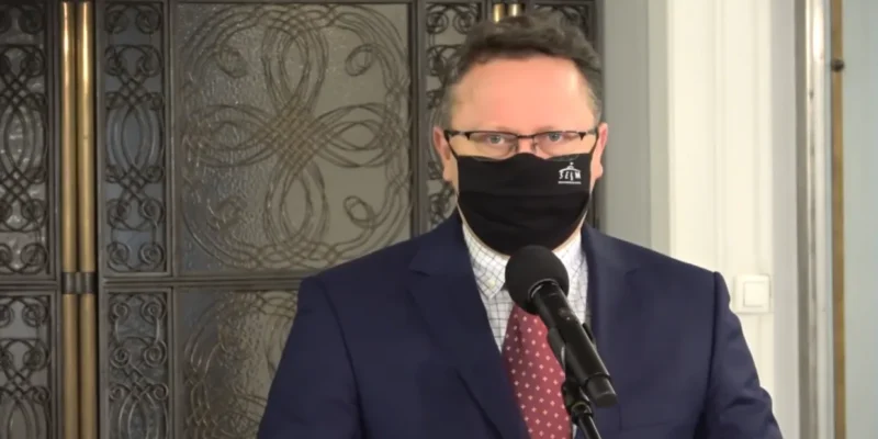 Mężczyzna w garniturze i maseczce stoi przy mikrofonie podczas konferencji prasowej.