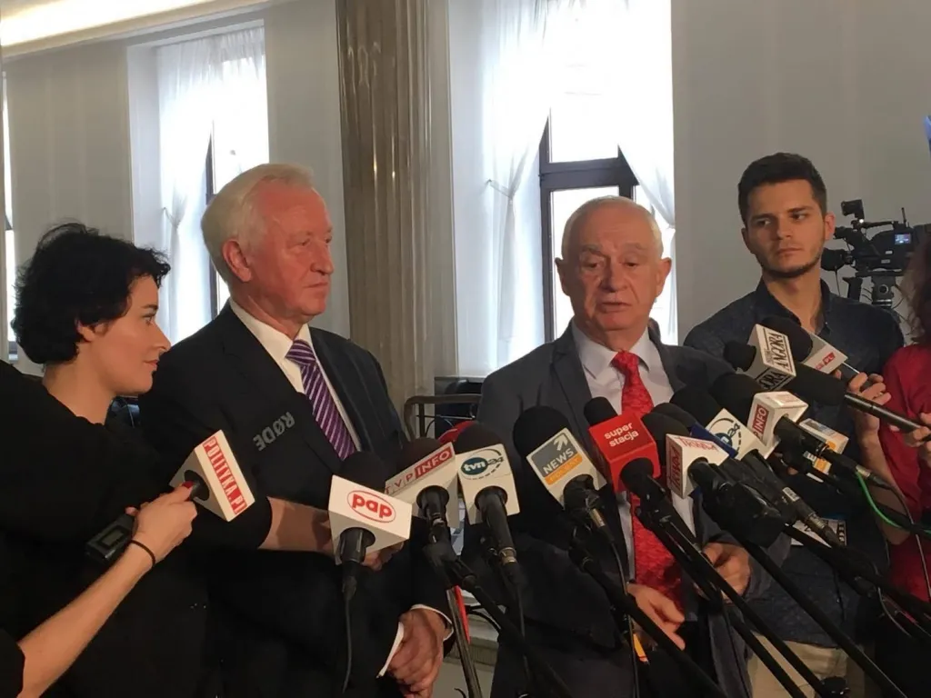 Polityk i współpracownicy stoją przed licznymi mikrofonami podczas konferencji prasowej o tym, że rząd nie sięga po środki UE na pomoc poszkodowanym w nawałnicach.