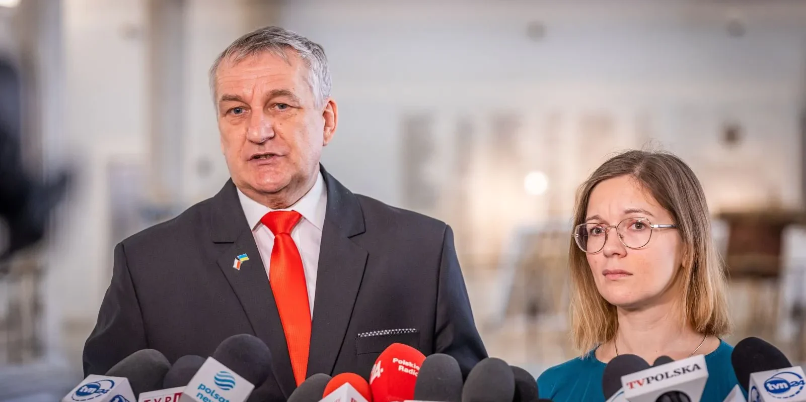 Na zdjęciu dwóch mówców stoi przed mikrofonami i kamerami podczas konferencji prasowej.