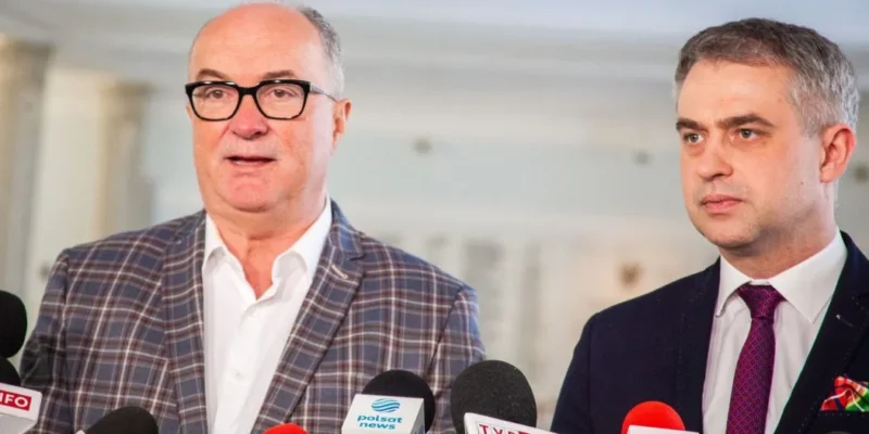 Dwóch mężczyzn w garniturach stoi przy mikrofonach podczas konferencji prasowej.