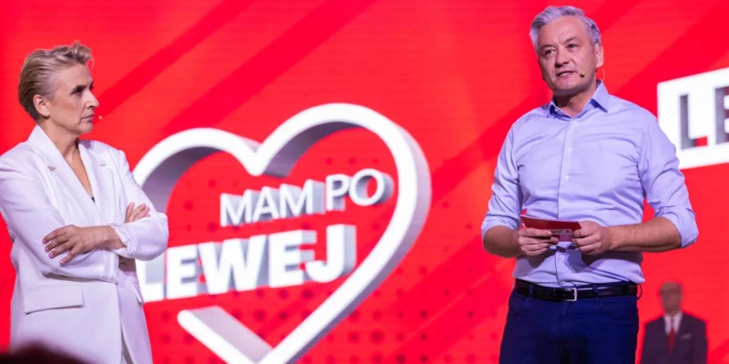 Dwóch prowadzących na scenie przed czerwonym tłem z sercem i napisem, kobieta w białej marynarce po lewej, mężczyzna w niebieskiej koszuli z mikrofonem po prawej, omawiają projekt związany z 35-godzinnym tygodniem pracy.