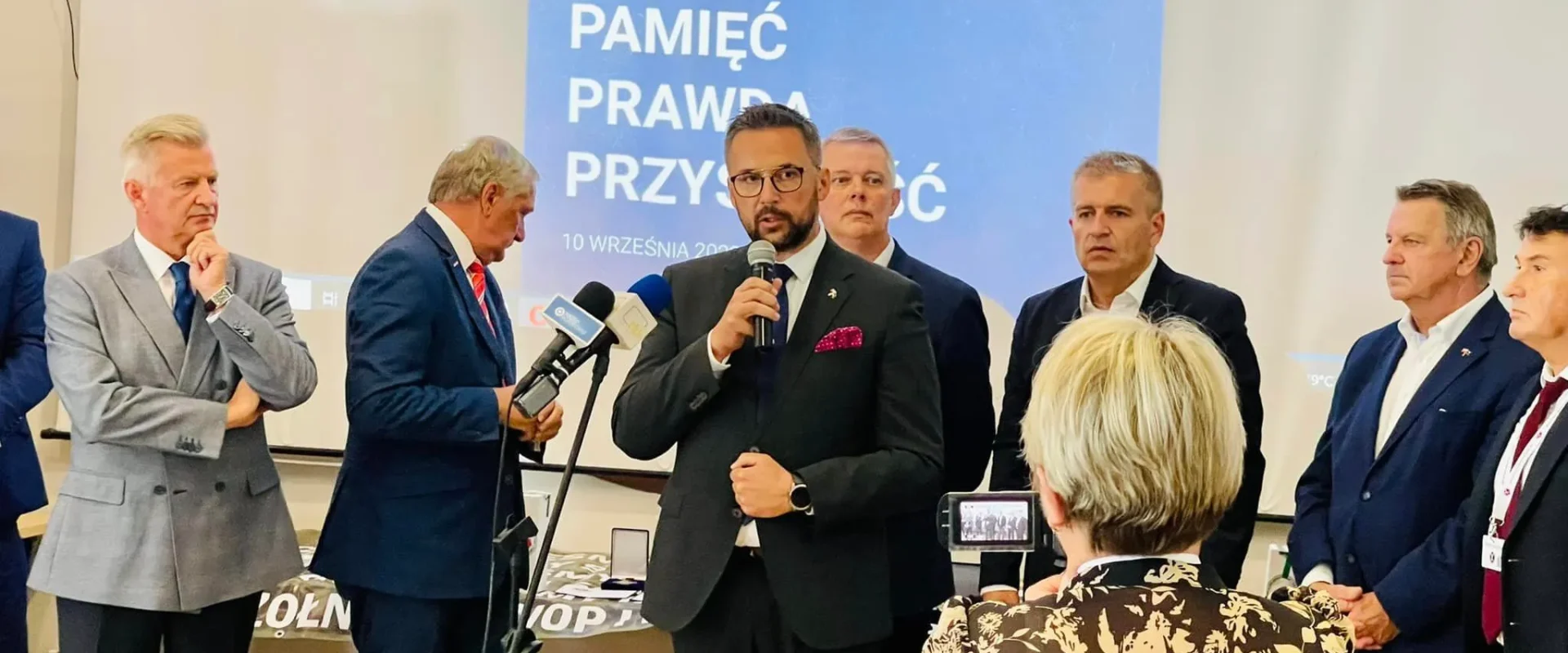 Na zdjęciu przedstawiono grupę uczestników IV Konferencji Służb Mundurowych, podczas gdy jeden z mówców przemawia do zgromadzonych gości.
