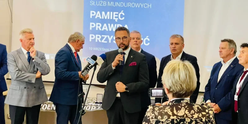 Na zdjęciu przedstawiono grupę uczestników IV Konferencji Służb Mundurowych, podczas gdy jeden z mówców przemawia do zgromadzonych gości.
