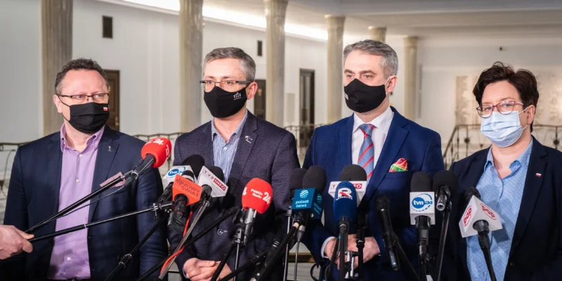 Czwórka polityków w garniturach, wszyscy w maseczkach, stoi przed zestawem mikrofonów podczas konferencji prasowej Rady Bezpieczeństwa Narodowego.