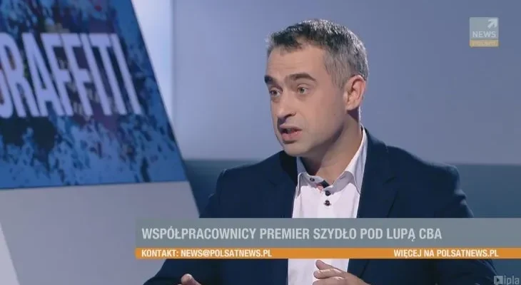 Mężczyzna w marynarce gestykuluje podczas wywiadu w studiu telewizyjnym, a na pasku informacyjnym widnieje napis "Współpracownicy premier Szydło pod lupą CBA".