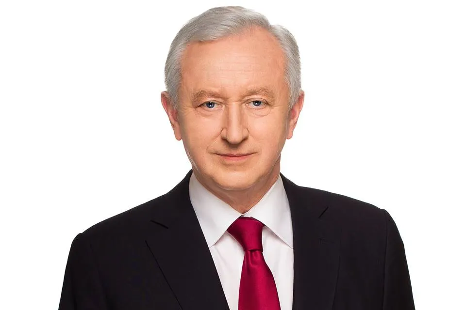 Portret mężczyzny w czarnym garniturze, białej koszuli i czerwonym krawacie na białym tle.