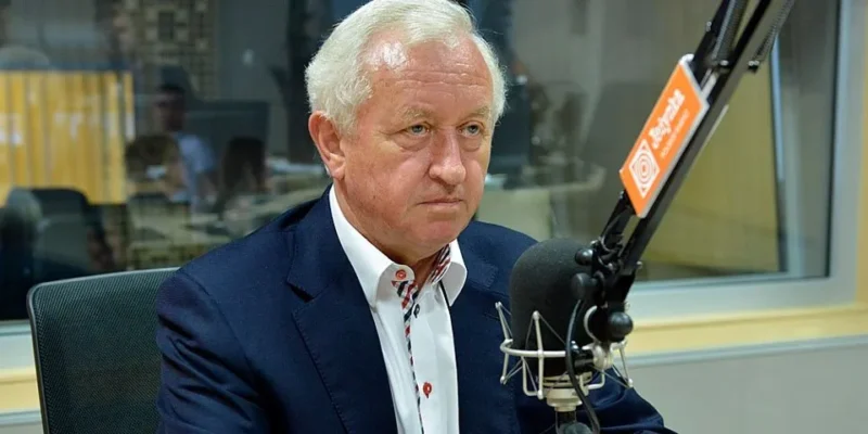 Starszy mężczyzna w eleganckiej marynarce siedzi w studiu radiowym i mówi do mikrofonu.