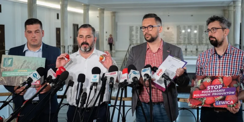 Czterech mężczyzn na konferencji prasowej Lewicy, trzymają plakaty dotyczące polskich truskawek i podrabiania produktów, stojąc za licznymi mikrofonami.