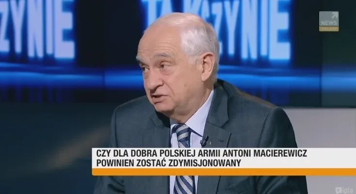 Starszy mężczyzna w garniturze wypowiada się w telewizyjnym studiu, a na pasku informacyjnym widnieje pytanie o dymisję Antoniego Macierewicza.